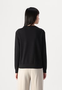 Maglione nero con una texture liscia, maniche lunghe e collo a giroclassico. Mostrato di spalle, abbinato a pantaloni color crema.