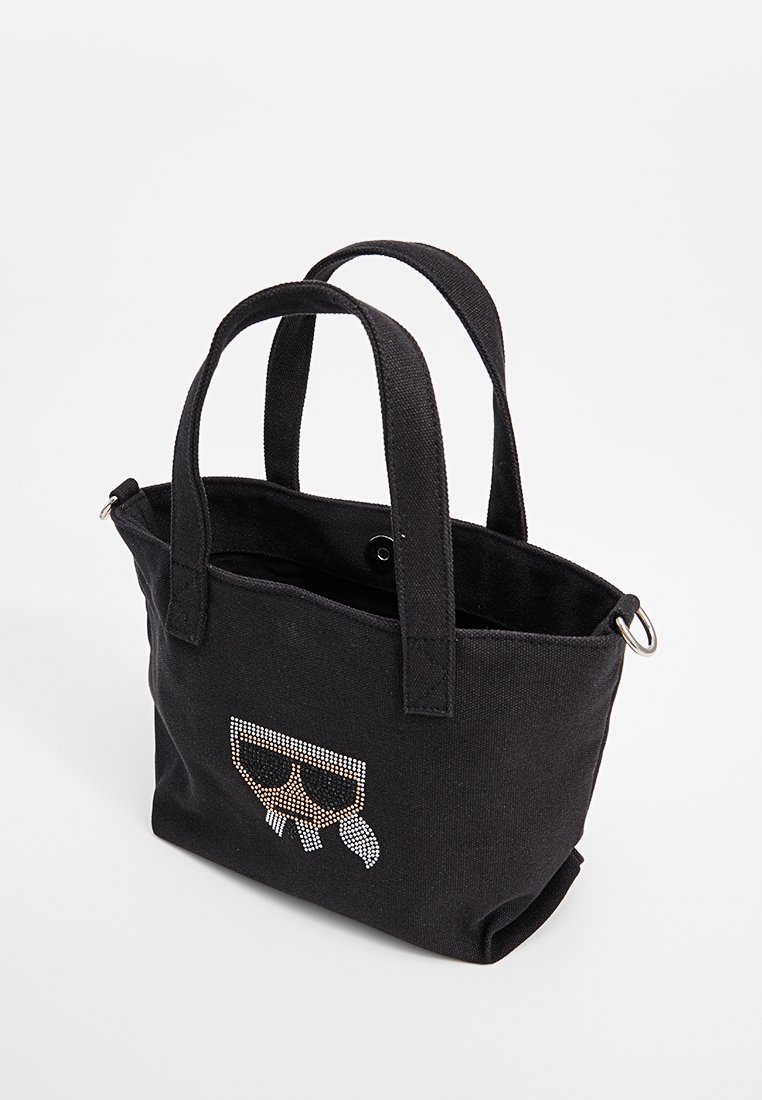 Sac fourre-tout noir en toile avec deux poignées, ornée d'un design en strass de lunettes sur le devant. Forme simple et structurée avec une fermeture à pression.