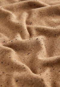 Brunt tekstureret stof med subtile sorte pletter, der viser en blød, ribbet udseende og krøllet overflade.