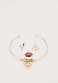Pulsera de oro con tres charms: un corazón con un cristal, labios rojos y una copa de cóctel con acento verde y cerezas. Acabado suave.