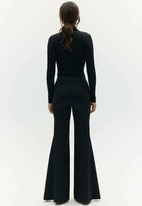 Zwarte, lange mouwen, fitted top in combinatie met hoge taille zwarte uitlopende broek, beide met een gladde textuur en consistente kleur.