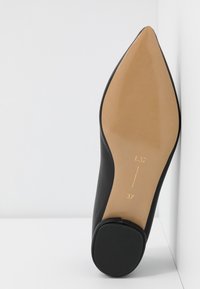 Chaussure à talon haut noire avec un bout pointu, une tige en cuir lisse et une semelle couleur tan. Présente des marquages dorés sur la semelle : L37 et 37.