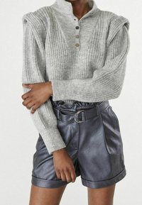 Grå, ribbad stickad tröja med halvknäppning och strukturerade axlar, ihopparad med svarta skinnshorts med bälte och öglor.