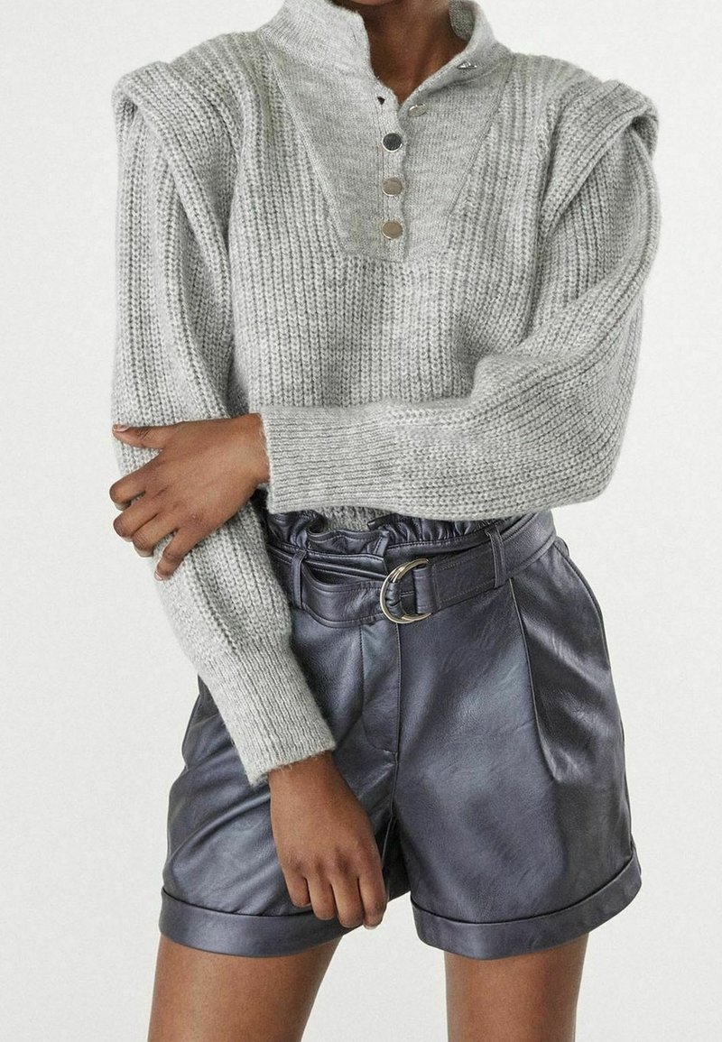 Grå, ribbad stickad tröja med halvknäppning och strukturerade axlar, ihopparad med svarta skinnshorts med bälte och öglor.