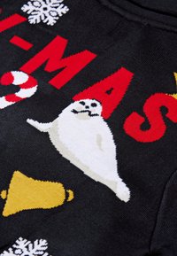 Tessuto nero con lettere rosse, fiocchi di neve bianchi, campana gialla, bastoncino di zucchero rosso e bianco e una foca bianca con un baffo.