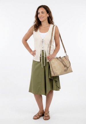 Donna che indossa un gilet lavorato a maglia crema senza maniche, canotta bianca, gonna midi verde oliva, sandali marroni, con borsa tote beige intrecciata sulla spalla.