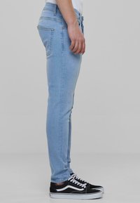 Világoskék skinny farmernadrág sima textúrával, hátizsebekkel és magas derekú fazonnal. Fekete-fehér tornacipővel párosítva.