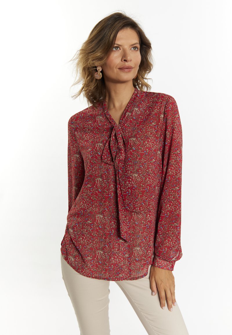 Blusa rossa a maniche lunghe con colletto a fiocco, caratterizzata da un motivo floreale in beige e blu. Realizzata in tessuto leggero e morbido.
