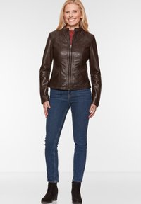 Braune Lederjacke mit tailliertem Schnitt, hohem Kragen und Frontreißverschluss. Kombiniert mit dunkelblauen Skinny-Jeans und schwarzen Ankle-Boots.