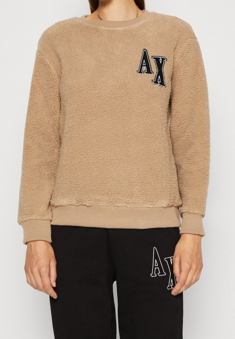 Felpa marrone chiaro in pile con scollo e polsini a coste. Presenta un logo "AX" nero ricamato sul petto e una finitura testurizzata.