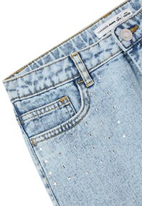 Jeans in denim blu chiaro con una consistenza sbiadita, una tasca frontale e decorati con borchie in argento nella parte inferiore.