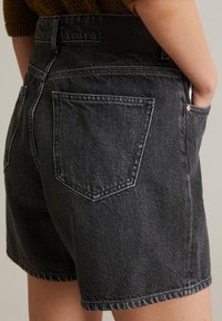 Zwarte denim shorts met een hoge taille, voorzien van twee achterzakken, gestikte details en een logopatch op de achterzijde van de tailleband.