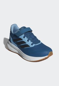 Scarpa sportiva blu con tomaia in mesh, dettagli neri, una fascia e una suola bianca ammortizzata con suola esterna in gomma color caffè. Progettata per il comfort.