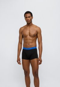 Μαύρα ανδρικά μποξέρ με μπλε ελαστική μέση που φέρει το κείμενο "TOMMY HILFIGER". Απλός σχεδιασμός χωρίς μοτίβα ή διακοσμήσεις.