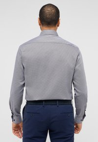 Langmouwshirt in een geweven blauw patroon, met een standaard kraag en knoopmanchetten, gedragen met donkerblauwe broek.