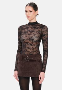 Zwarte kanten bodysuit met lange mouwen en bloemmotieven, gecombineerd met een bruine suède minirok met een brede riem en een ronde gesp als detail.