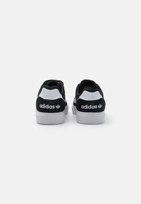 Black and white suede sneakers with a textured upper, white rubber sole, and an embroidered adidas logo on the heel.