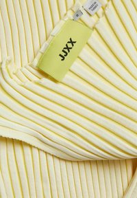 Tissu côtelé jaune doux avec étiquettes de vêtements indiquant la marque "JJXX", la taille "S" et l'étiquette "Fabriqué en Turquie".