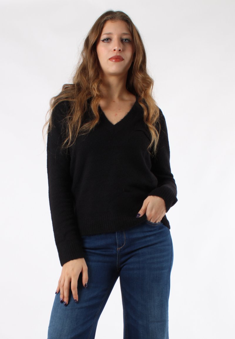 Maglione nero a collo a V realizzato in un morbido tessuto testurizzato, abbinato a jeans blu. Il maglione presenta polsini e orlo a costine.