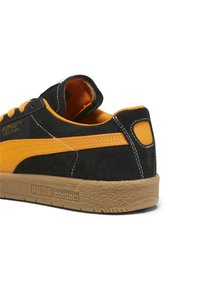 Sneaker in suede nero e arancione con suola in gomma texturizzata, caratterizzata da cuciture a contrasto e una collana imbottita per il comfort.