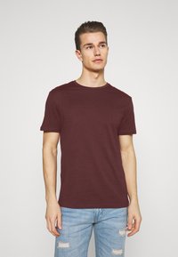 Burgunderrød t-skjorte med korte ermer laget av bomull, med rund hals og slim fit, kombinert med lyse, slitte denimjeans.
