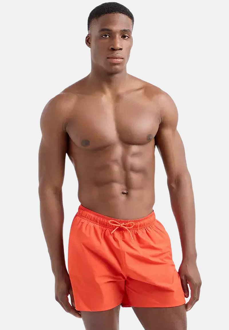 Bañador naranja con cinturilla elástica y cordón, hecho de material ligero. Presenta una textura suave y un corte holgado.
