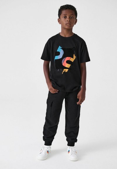 Musta puuvillapaita, jossa on värikäs grafiikkasuunnittelu edessä. Yhdistetty mustiin cargo-housuihin ja valkoisiin lenkkareihin, joissa on sateenkaaren sävyjä.