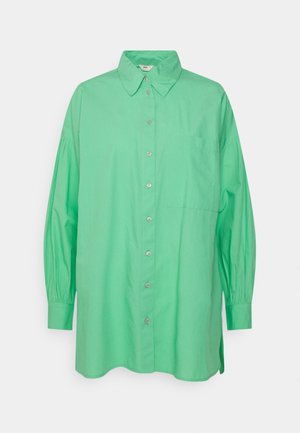 Losse groene blouse met lange mouwen, knopen en een puntige kraag, met een borstzak, weergegeven op een witte achtergrond.