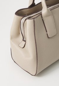 Beige leather handbag with a textured surface, featuring contrasting dark trim and a zip closure. Rounded shape with short handles.