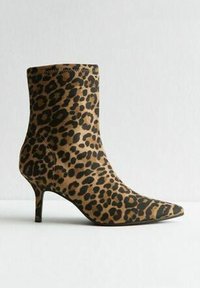 Botín de tobillo con estampado de leopardo, punta afilada, diseño ajustado, tejido texturizado y un tacón delgado y curvado. La combinación de colores incluye marrón y negro.