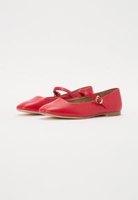Bailarinas de cuero rojo con punta afilada, que presentan una correa delgada en el tobillo y un tacón bajo de madera. Textura suave con acentos mínimos.
