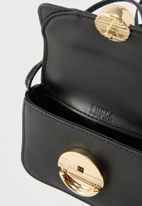 Melna ādas rokas soma ar apaļu zelta aizdares sprādzi, gluda tekstūra un iegravēts zīmola logotips iekšpusē. Kompakts un strukturēts dizains.