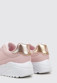 Różowe sneakersy z gładką cholewką, perforowanymi akcentami, metalicznie złotą pętelką na pięcie oraz białą, teksturowaną podeszwą z falistym wzorem.