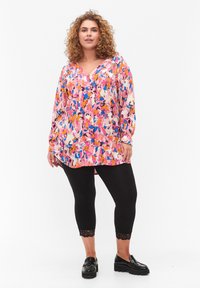 Blouse à manches longues dans un rose vibrant et un motif abstrait multicolore, associée à des leggings noirs avec une finition en dentelle à l'ourlet.