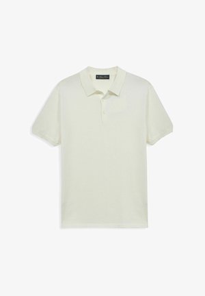 Roomkleurig polohemd met korte mouwen, kraag en drie knopen, plat uitgestald op een witte achtergrond.