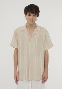 Camicia beige a maniche corte con strisce bianche verticali, tessuto leggero e chiusura frontale con bottoni. Presenta un classico design con colletto.