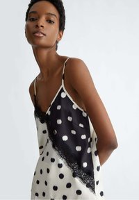 Camisola a pois bianco e nero con bordo in pizzo. Tessuto elegante, spalline regolabili e un design a motivi su sfondo crema.