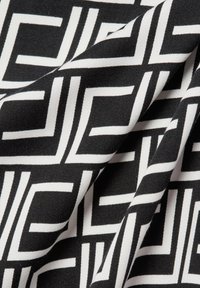 Schwarzer und weißer Stoff mit einem geometrischen Muster aus ineinandergreifenden Rechtecken, gefaltet, um Textur und Tiefe zu zeigen.