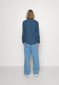 Camisa de cuadros azul de manga larga combinada con pantalones de mezclilla azules holgados. El conjunto presenta un ajuste relajado y un estilo casual.