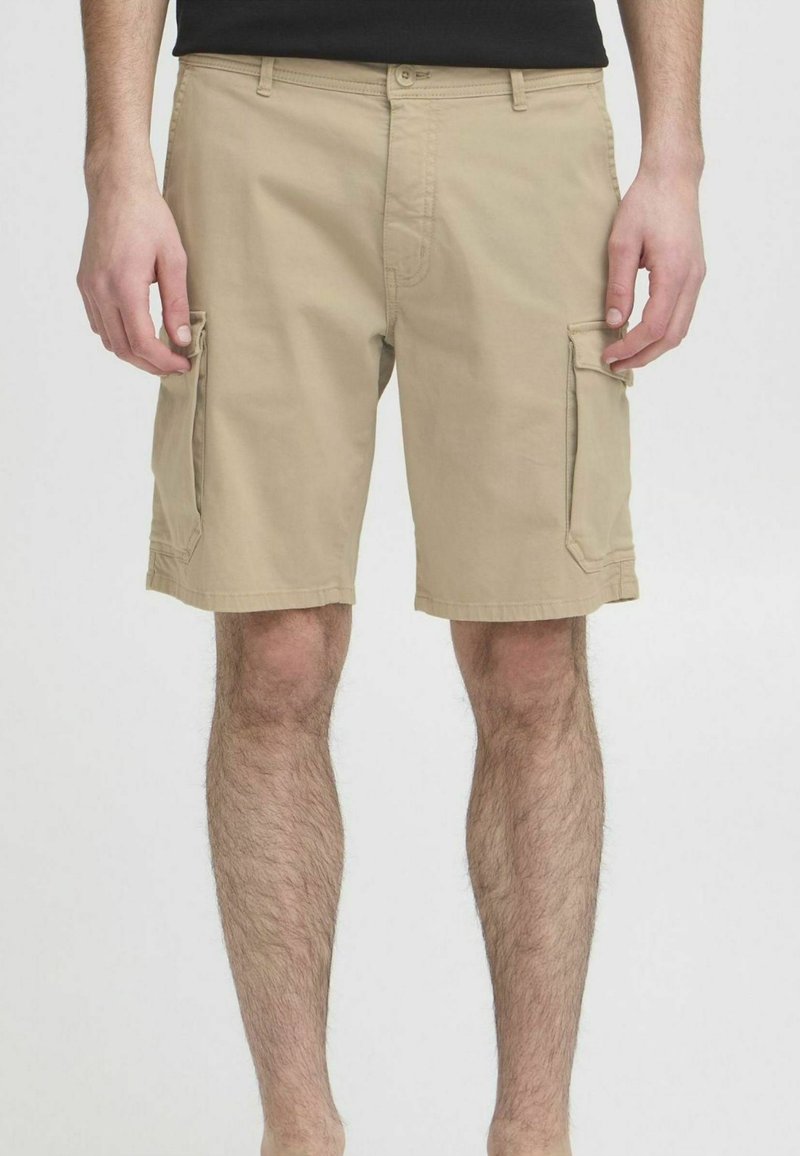 Shorts cargo beige mi-genou avec poches à rabat de chaque côté portés par une personne portant un t-shirt noir.
