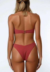 Set bikini in un colore terracotta opaco; top bandeau con chiusura sul retro, slip alte con copertura minima e texture liscia.