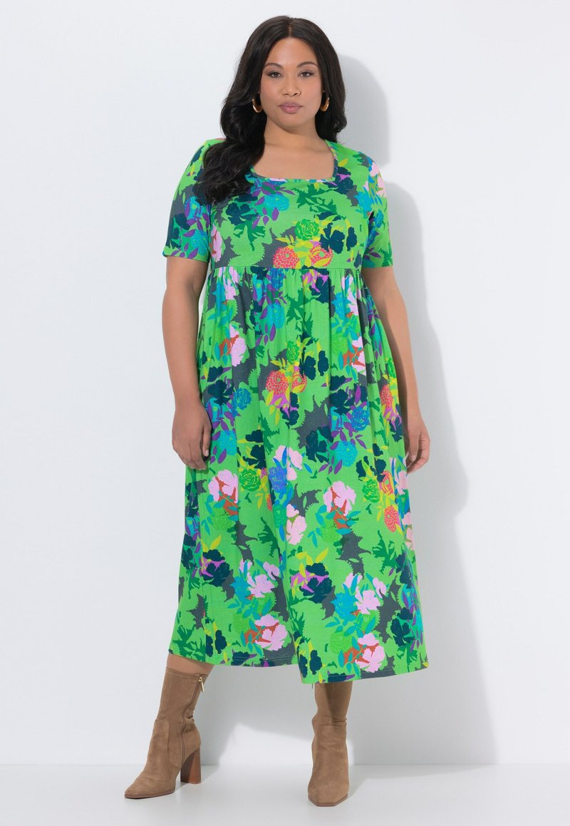 Woman wearing a colorful green floral midi dress with short sleeves and square neckline, paired with tan high-heeled suede ankle boots.
