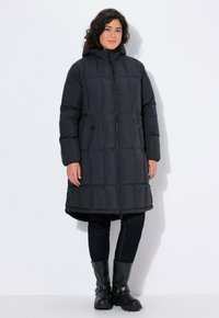 Svart pufferjacka med huva, med en quiltad design, dragkedjest�ängning och sidofickor. Bärs över mörka jeans och svarta läderstövlar.