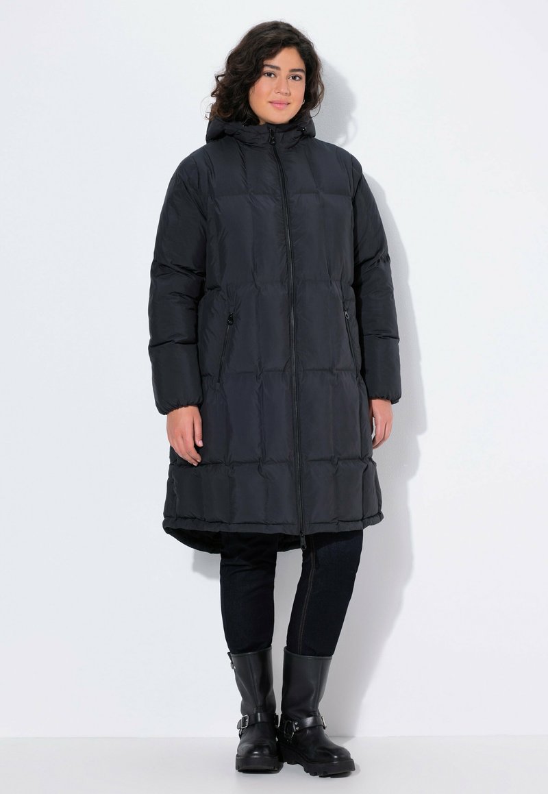 Svart pufferjacka med huva, med en quiltad design, dragkedjestängning och sidofickor. Bärs över mörka jeans och svarta läderstövlar.
