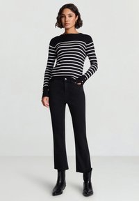 Schwarz-weiß gestreifter Pullover mit langen Ärmeln, schwarze ausgestellte Jeans und schwarze Stiefeletten. Gestrickte Textur, figurbetontes Design und Knopfdetails an den Ärmeln.