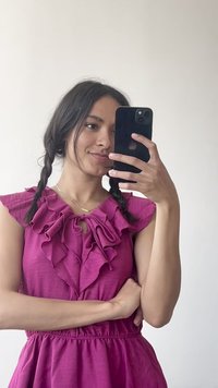 Robe fuchsia avec un col en volants et une taille froncée. Le mannequin tient un téléphone. L'arrière-plan est blanc uni, mettant en valeur les détails de la tenue.