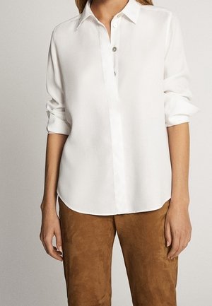 Witte knopen-overhemd met een kraag, voorzien van een voorpaspel en opgerolde mouwen, gecombineerd met bruin suède broeken. Glad van textuur.