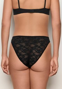 Schwarzer Spitzenstring mit floralem Muster, halbtransparentem Material und hohem Schnitt. Verstellbare Träger am passenden schwarzen BH.