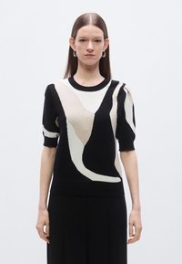 Pletený sveter s abstraktným béžovo-čiernym vzorom, krátkymi nafúknutými rukávmi, okrúhlym výstrihom a mäkkou textúrou. Minimalistický dizajn s kontrastnými farbami.