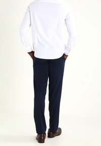 Witte shirt met lange mouwen, marineblauwe broek, bruine schoenen. Het shirt heeft knoopmanchetten; de broek is op maat gemaakt met een gladde afwerking. Eenvoudig ontwerp.